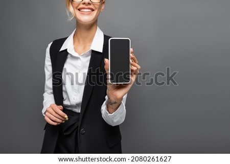 Cropped view of smiling businesswoman showing smartphone with blank screen isolated on grey