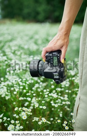 Female photographer holding a camera outdoors on flower field landscape, unrecognizable woman hold digital 
camera in her hands. Travel nature photography,  space for text.