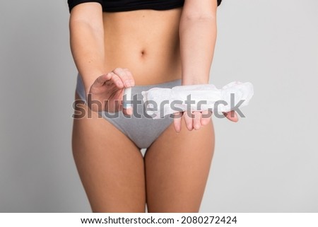 Alternative of products for intimate hygiene. Closeup of woman body in gray underwear holds sanitary pad and tampon. Gray background free space for text. Female intimate hygiene concept.