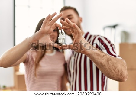 Young caucasian couple doing heart symbol with fingers and holding key of new home.