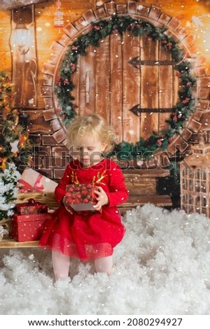 Cute little blond child, curly girl, sitting in wooden cabin with christmas decoration, opening presents, happy childhood