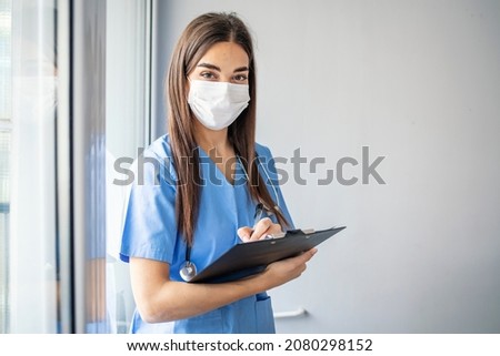 Happy nurse working at the hospital. Portrait of a happy Latin American nurse working at the hospital and looking at the camera smiling. Nurse with N95 face mask going through medical reports  Royalty-Free Stock Photo #2080298152