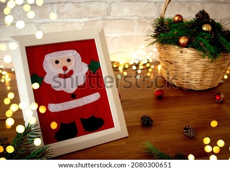 image of Santa Claus in a white frame, blurry specks of garlands, next to the branches of a Christmas tree, New Year's decorations in a wicker basket, a festive mood and DIY crafts family traditions