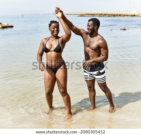 Young african american tourist couple wearing swimwear dancing at the beach.