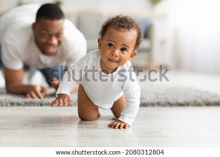 Cute Little Black Infant Baby Crawling On Floor At Home, Proud Young Father Looking At Him And Smiling, Dad And Toddler Child Enjoying Spending Time Together, Selective Focus With Copy Space Royalty-Free Stock Photo #2080312804