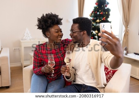 Beautiful young couple in love spending Christmas night at home and drinking champagne. Joyful couple clinking champagne glasses and making selfie. Holidays celebrations family together