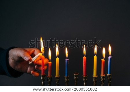 Jewish Holiday Hanukkah concept. Man lighting candles for Hannukah, traditional festival of lights on dark background
