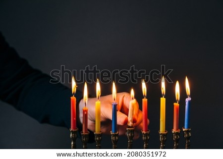 Jewish Holiday Hanukkah concept. Man lighting candles for Hannukah, traditional festival of lights on dark background