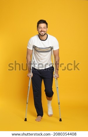Man with injured leg using crutches on yellow background Royalty-Free Stock Photo #2080354408