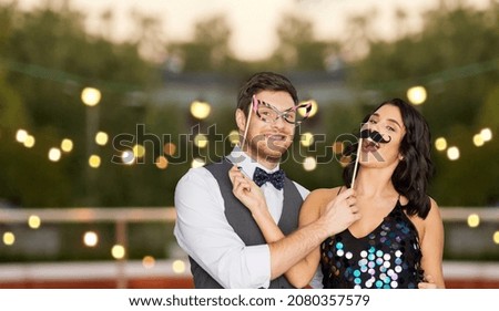 celebration, fun and holidays concept - happy couple posing with party props on roof top over lights on background