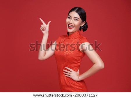 Happy Asian woman wearing traditional cheongsam qipao dress hand pointing up to copy space isolated on red background. Happy Chinese new year Royalty-Free Stock Photo #2080371127