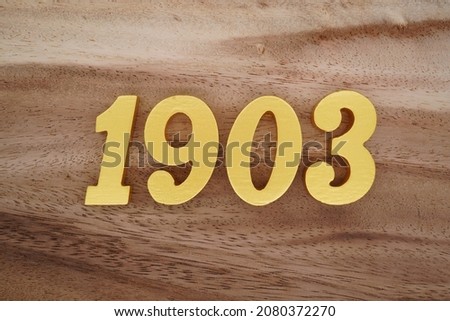 Golden Arabic numerals 1903 on a dark brown to white wood grain background.