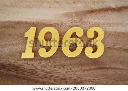 Golden Arabic numerals 1963 on a dark brown to white wood grain background.