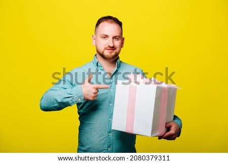 happy handsome bearded man giving a christmas gift, on yellow background. nice male holding gift box isolated on yellow, international womens day concept