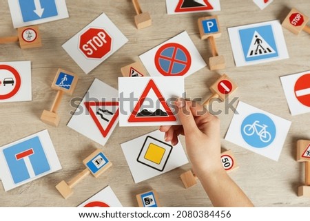 Woman holding rough road sign over wooden table, top view. Driving license exam
