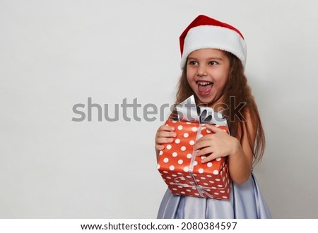 Cute girl with christmas gift box on a white background with copy space. Portrait of a 5 years old girl wearing white dress and Santa hat 