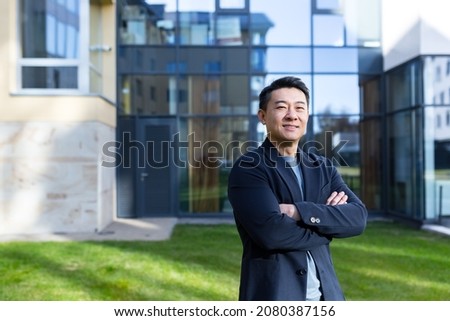 portrait handsome Asian man a university college teacher, businessman, scientist or educator. Standing background modern office center or campus with arms crossed Outside, outdoors looking at camera