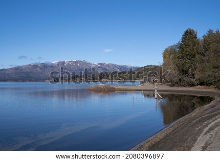 View of the lake shore, beach, forest and blue water lake in a summer sunny day. The alps and mountains in the background. Royalty-Free Stock Photo #2080396897