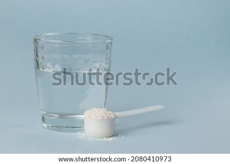 Mineral supplement diatomaceous earth or diatomite powder in a plastic spoon. White powder in a scoop and glass of water for preparation of the detox drink Royalty-Free Stock Photo #2080410973