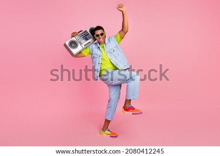Full size photo of funky young guy dance with boom box wear eyewear vest t-shirt jeans sneakers isolated on pink background