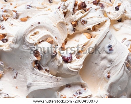 Frozen Hazelnut flavour gelato - full frame detail. Close up of a white creamy surface texture of Ice cream filled with pieces of nuts. Royalty-Free Stock Photo #2080430878