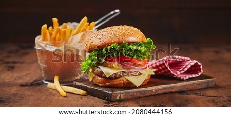 Homemade burger with beef, cheese and onion marmalade on a wooden board, fries in a metal basket. Fast food concept, american food. Long wide banner Royalty-Free Stock Photo #2080444156