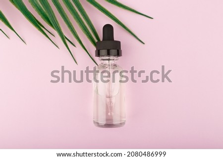 Skin serum in transparent bottle on bright pastel purple background with palm leaf and copy space. Concept of anti aging or anti acne organic, natural skin treatment for glowing, young looking effect