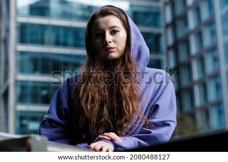 Portrait of a young woman in a purple hooded sweat, financial environment. Moody image in London financial district.