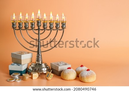 Image of Jewish holiday Hanukkah with menorah (traditional Candelabra), donuts and wooden dreidels (spinning top), chocolate coins on Coral background.