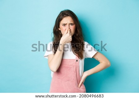 Portrait of bothered cute girl shut nose and frown from bad smell, smelling terrible reek, something stink, standing against blue background Royalty-Free Stock Photo #2080496683