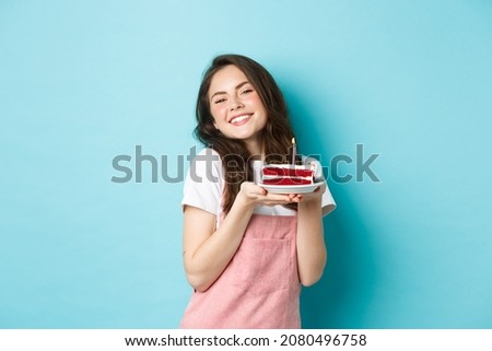 Holidays and celebration. Cute glamour girl celebrating her birthday, holding plate with cake and smiling cheerful, celebrating, standing over blue background
