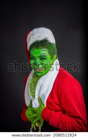 man dressed as christmas green, sitting in studio black background with santa claus suit