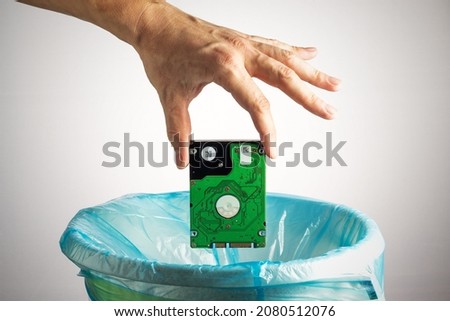 Person's hand throws a computer hard disk into the trash bin. Loss of information, obsolescence of computer technology, concept
