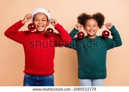 Photo of two funny cute kids brother sister hold tree baubles wear x-mas hat jumper isolated beige color background