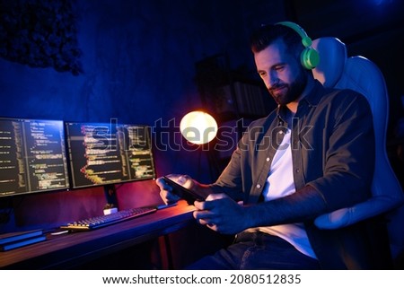 Portrait of positive handsome guy sit chair play games earphones melody song pause break night dark room indoors Royalty-Free Stock Photo #2080512835