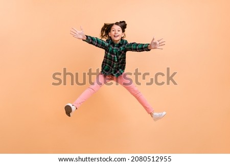 Photo of funny excited schoolgirl wear plaid outfit jumping high hands legs sides smiling isolated beige color background