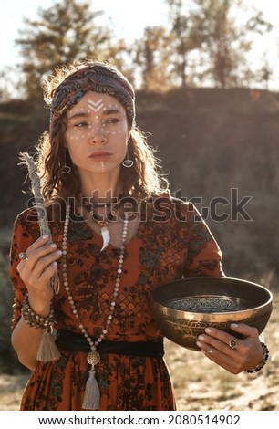 A woman in a turban holds burning incense in her hands, dancing in nature in the rays of the setting sun