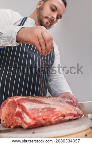 Cook sprinkles with spices a piece of meat. On the front of picture is his hand and meat.