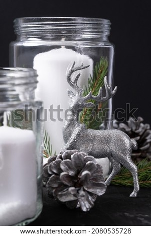 Silver Christmas deer on the background of candles and cones on black background. Close up.