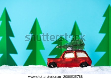 Red small car in the snow with cartoon paper trees background. Copy space. Childish postcard concept