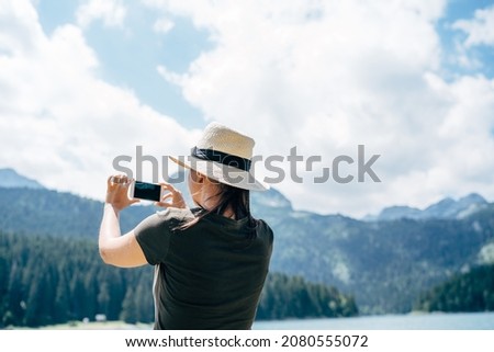 Woman is taking pictures of the mountains on her phone. Back view