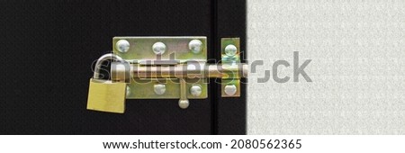 Metal brass gold door padlock, lock and bolt on the black metal door and white stucco wall background, close up. Banner.