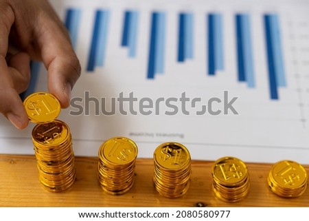 Business ideas, money, savings, and security. Close-up of a man holding a coin on a pile of coins on a table with graphs of finances.