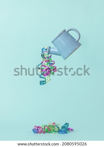 A blue watering can with a serpentine pouring out of it on a light blue background. The minimum concept of the New Year. Contemporary art. Place for text.