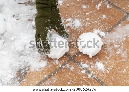 Winter fun. A hand in a green glove puts a snow globe on the street paving slabs close-up. Nearby lies the second lump


