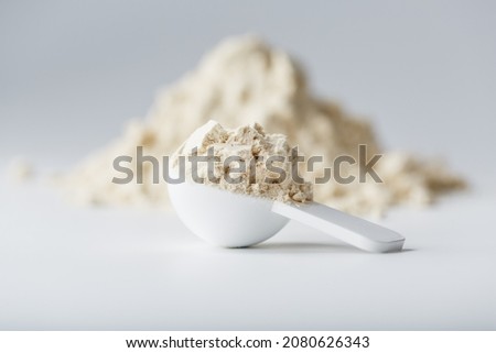 A mountain of soy protein isolate in powder with a measuring spoon on a white background. Vegetarian sports nutrition for cocktails Royalty-Free Stock Photo #2080626343