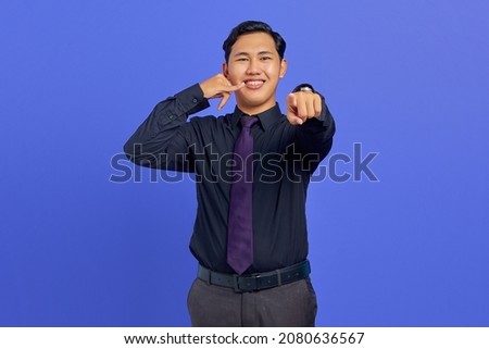 Portrait of attractive Asian man make call gesture sign and pointing at camera over purple background