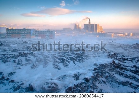 Winter arctic industrial landscape. View of the thermal power plant and residential buildings of the northern town. Cold snowy and windy weather. Blowing snow. Polar climate. Anadyr, Chukotka, Russia. Royalty-Free Stock Photo #2080654417