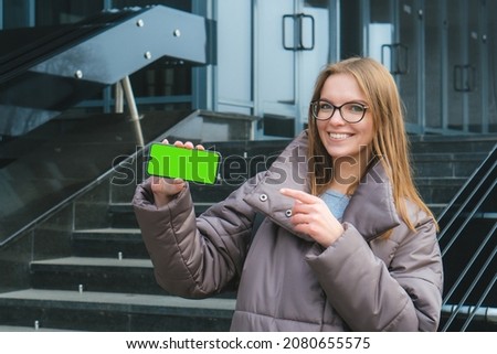 Beautiful smiling caucasian girl with glasses showing blank smart phone green screen