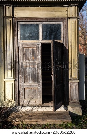 Historical wooden house with opened old wooden doors and windows at the top. Stairs are visible behind the door. Kuldiga, Latvia.